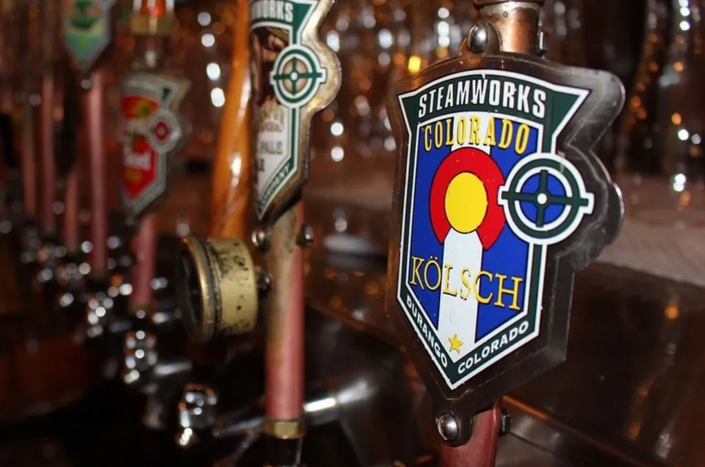 A row of bright beer taps at a Colorado craft brewery taproom with exposed brick walls and warm industrial lighting.