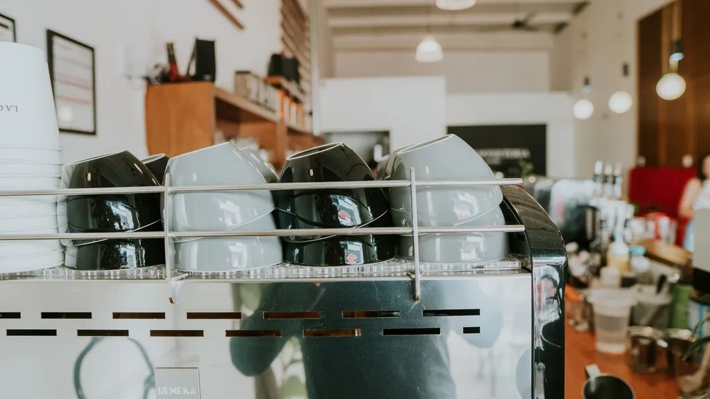 The bright interior of a local coffee shop, with an espresso machine and stacked cups along the counter.